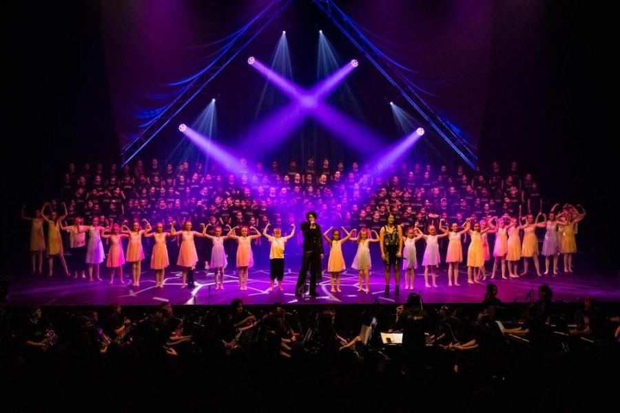 A large group of people are standing on a stage with purple lights.