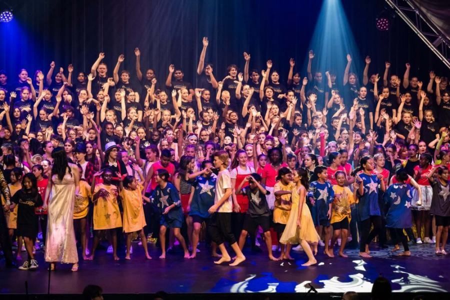 A large group of children are dancing on a stage.