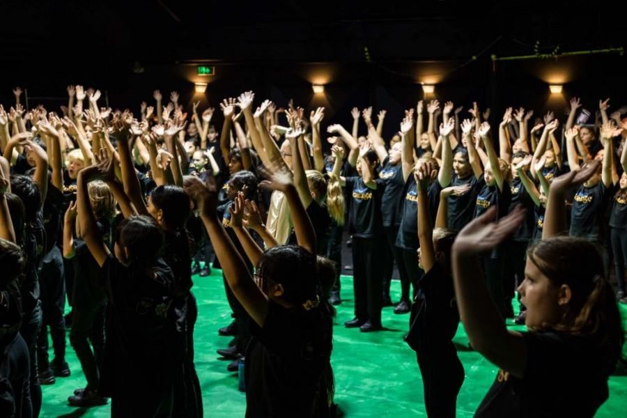 A large group of people are standing in a dark room with their hands in the air.