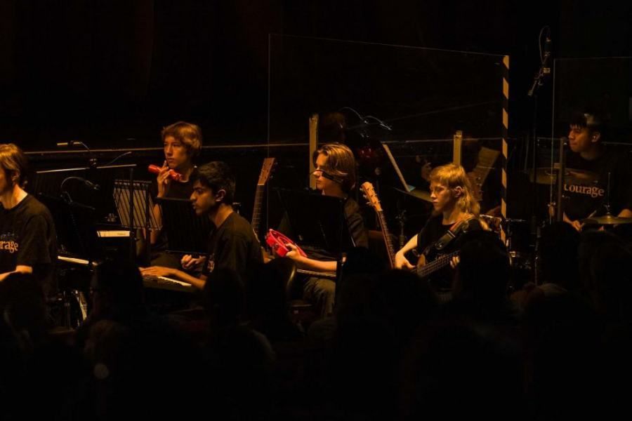 A group of people are playing instruments on a stage in a dark room.