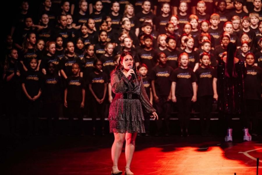 A woman is singing into a microphone in front of a large choir.
