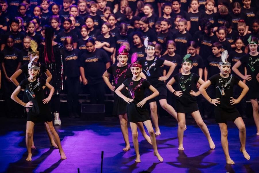 A group of young girls are dancing on a stage in front of a large choir.