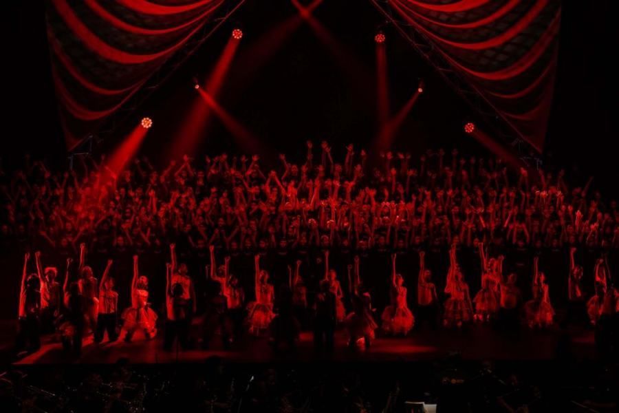 A large group of people are standing on a stage in front of a red curtain.