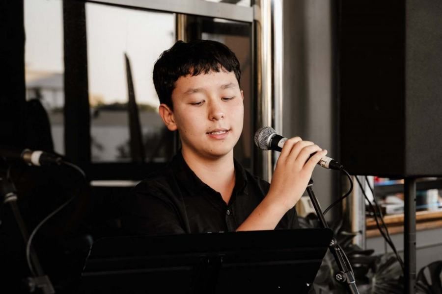A young boy is singing into a microphone while sitting at a piano.