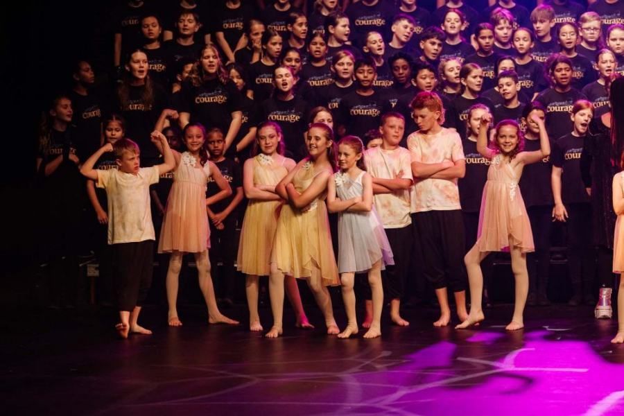 A group of children are standing on a stage with their arms crossed.