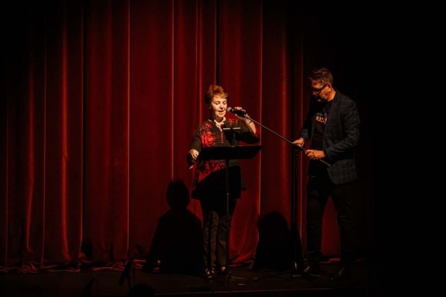 A man and a woman are standing on a stage in front of a red curtain.