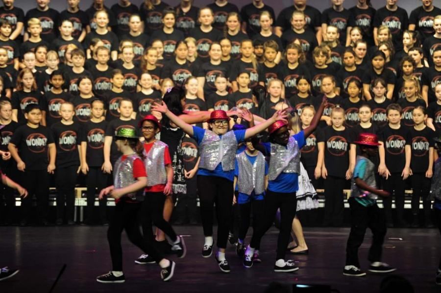 A group of children are dancing on a stage in front of a large choir