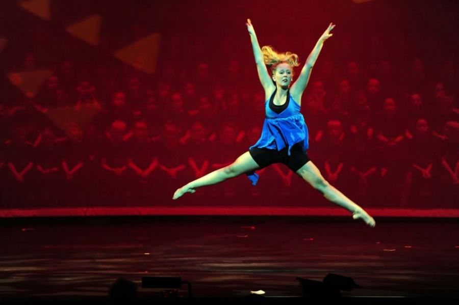 A woman in a blue dress is jumping in the air on a stage.