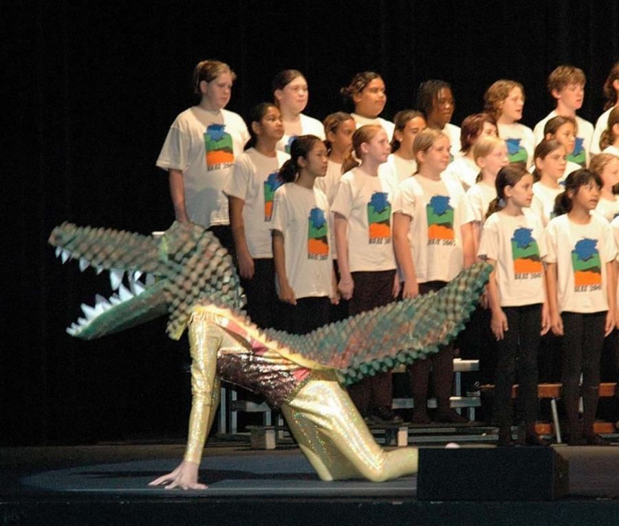 A group of children are singing in front of a crocodile costume