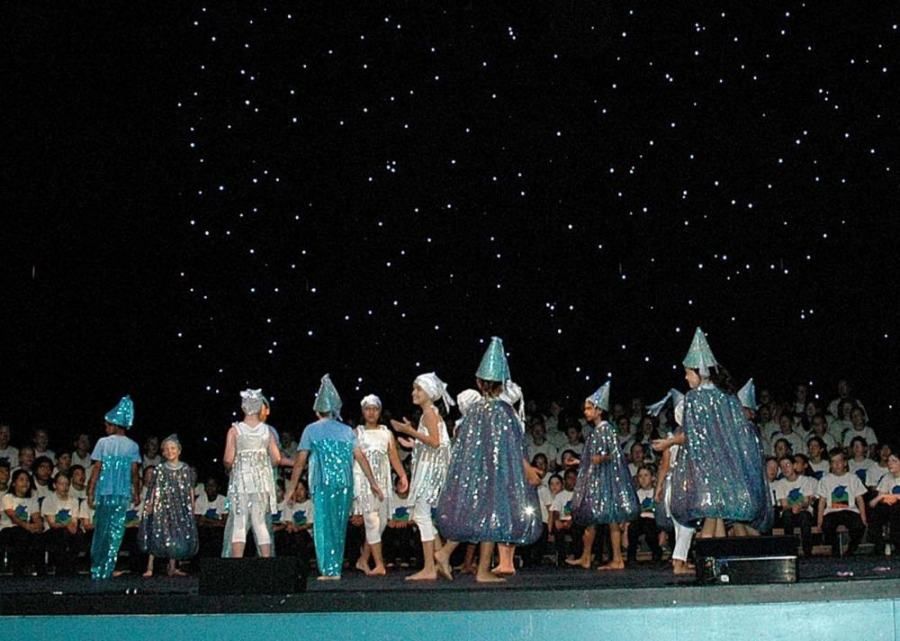 A group of children are dancing on a stage in front of a crowd