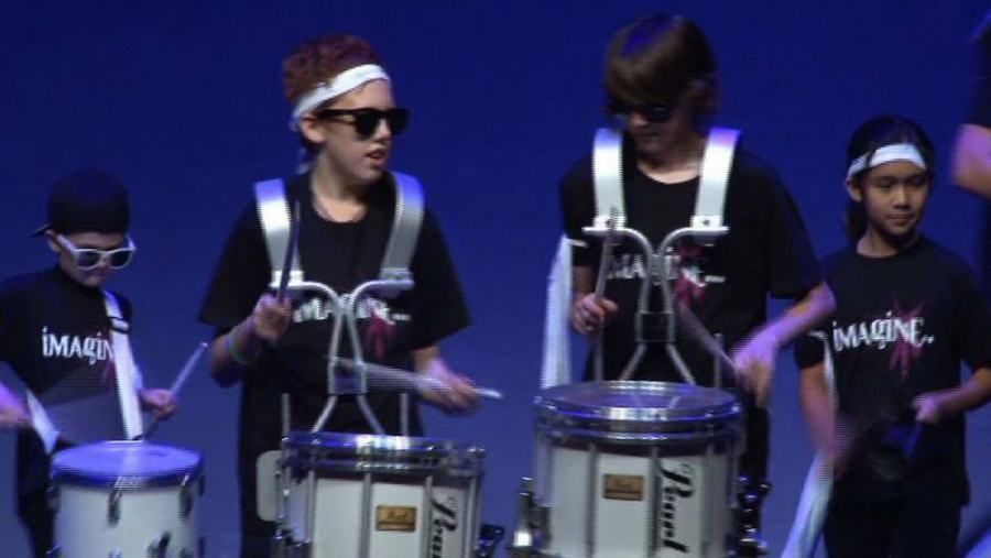A group of young boys are playing drums and wearing pearl shirts