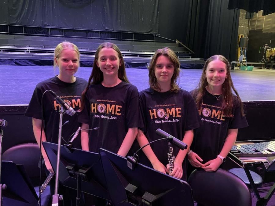 A group of young girls wearing black shirts that say home are standing in front of a stage.