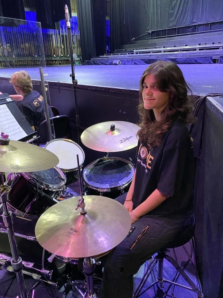 A young girl is sitting in front of a drum set on a stage.