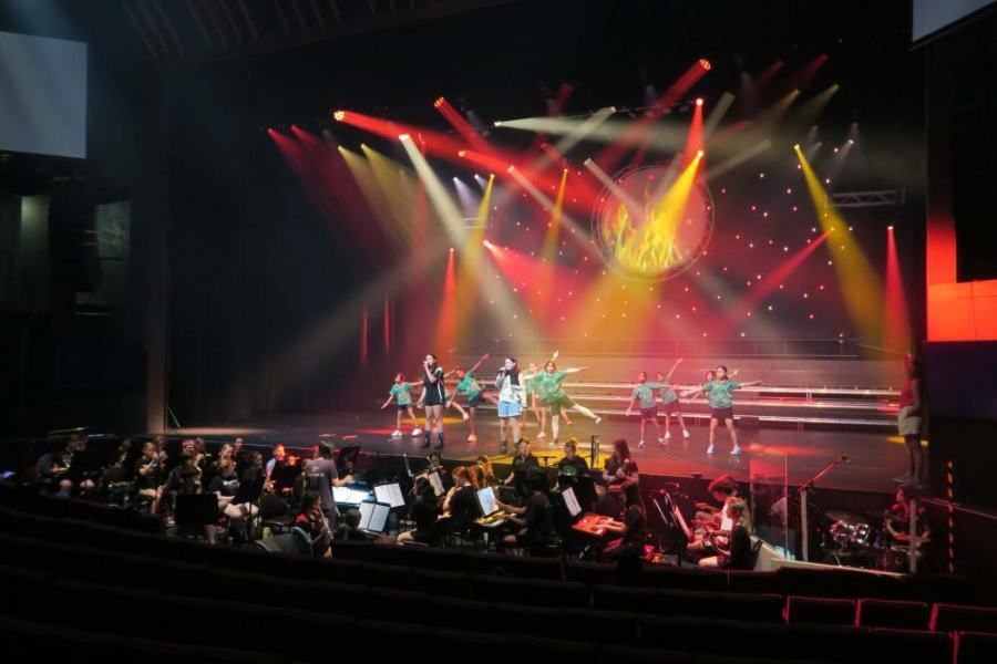 A group of people are dancing on a stage in front of an orchestra