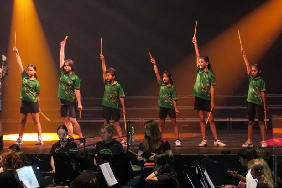 A group of children are standing on a stage holding sticks in the air.