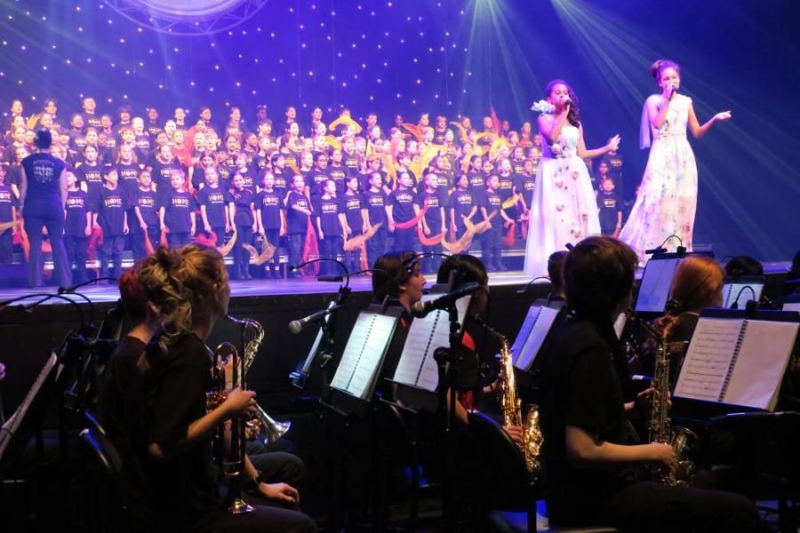 A group of people are playing instruments on a stage in front of a large choir.