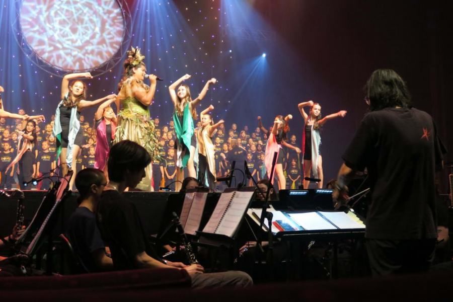 A group of people are dancing on a stage while a man plays a guitar.