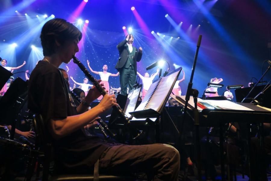 A man is playing a flute in front of an orchestra