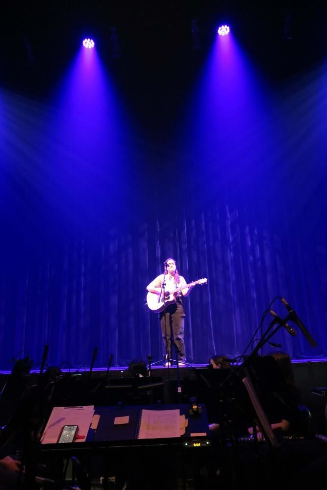 A man is playing a guitar on a stage with purple lights