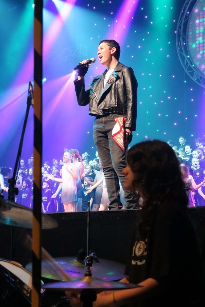 A man in a leather jacket is singing into a microphone on a stage