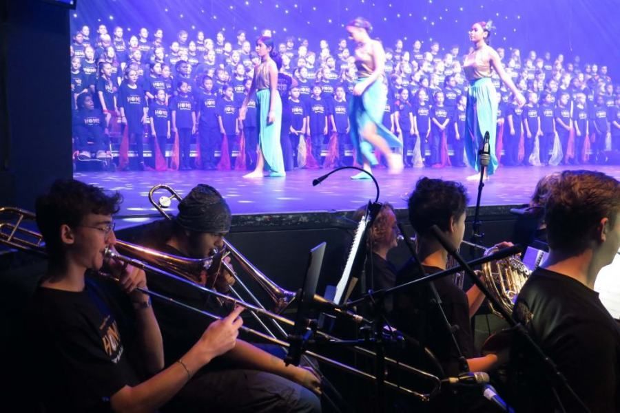 A group of people are playing instruments in front of a large screen.
