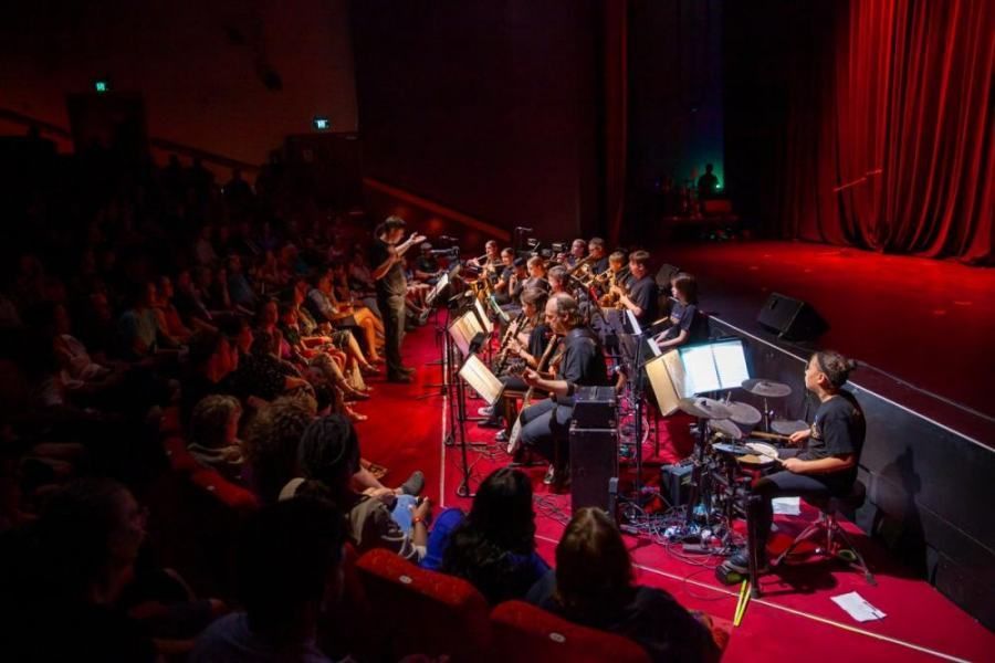 A large orchestra is playing on a stage in front of a crowd of people.