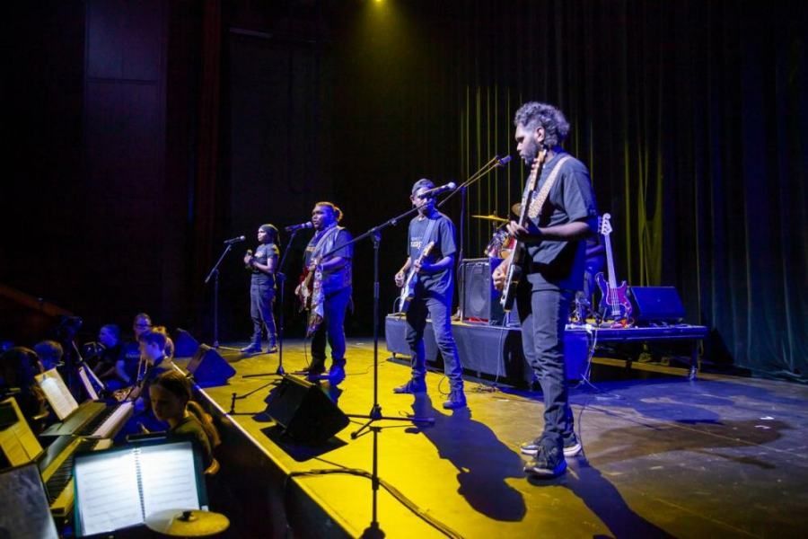 A group of men are standing on a stage playing guitars and singing into microphones.