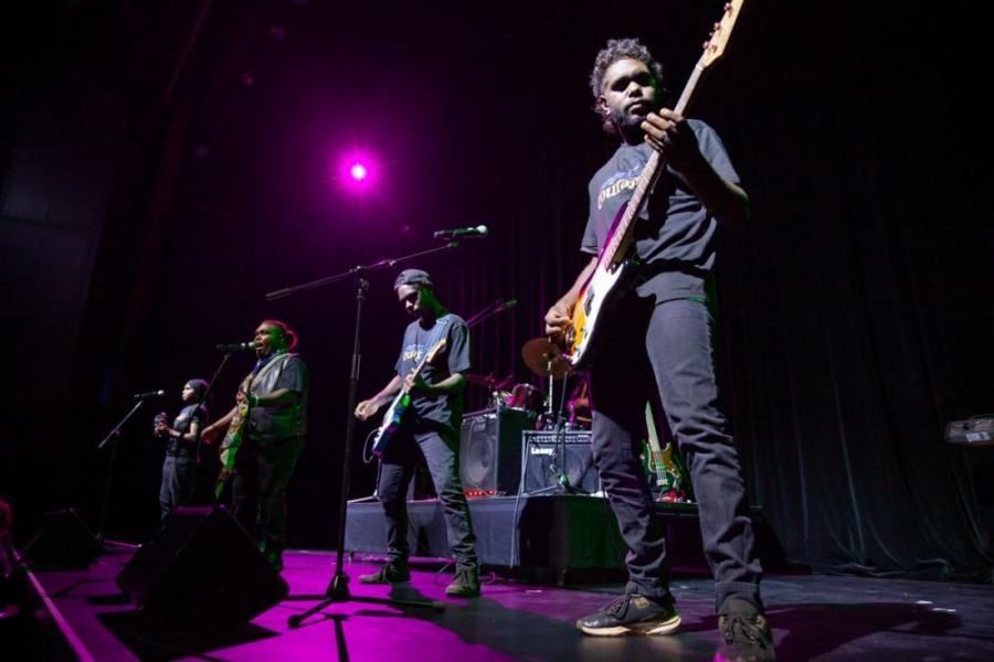 A group of people are standing on a stage playing guitars and singing into microphones.