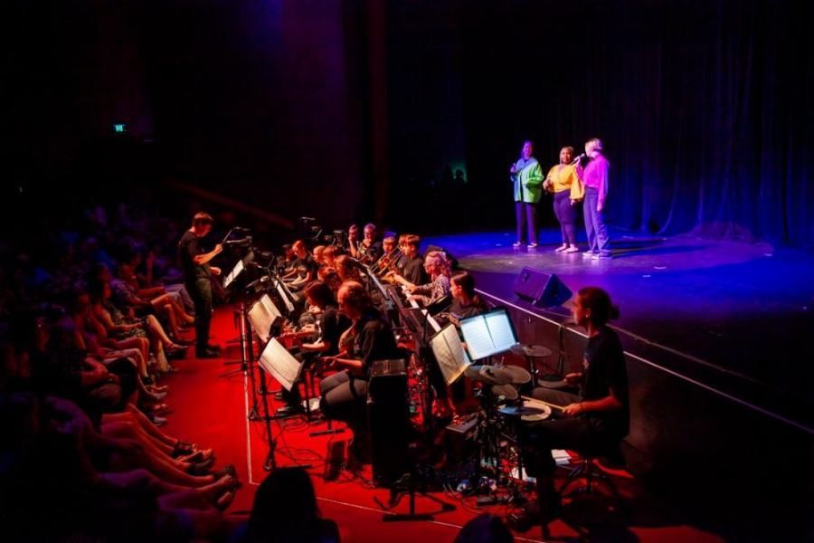 A man is playing drums on a stage in front of an orchestra.