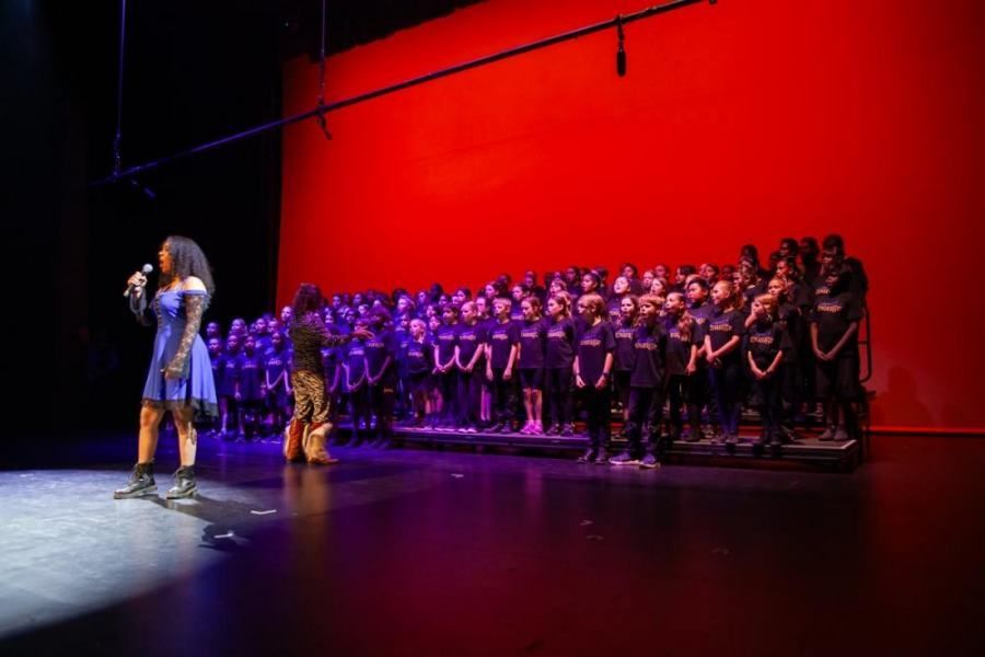 A woman is singing into a microphone on a stage in front of a large choir.