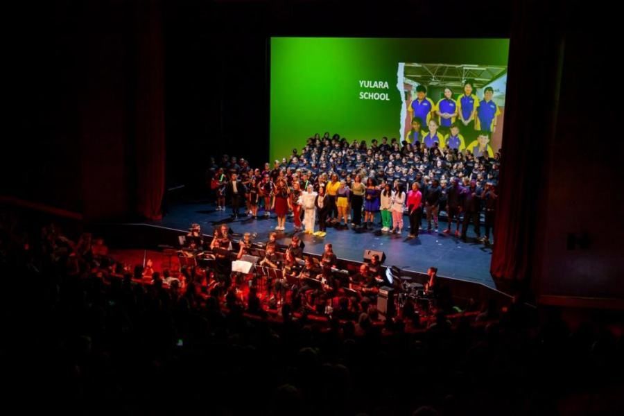 A large group of people are standing on a stage in front of a large screen.