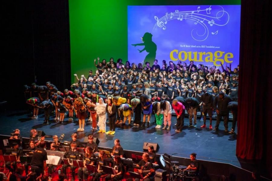A large group of people are standing on a stage in front of a large screen that says courage.