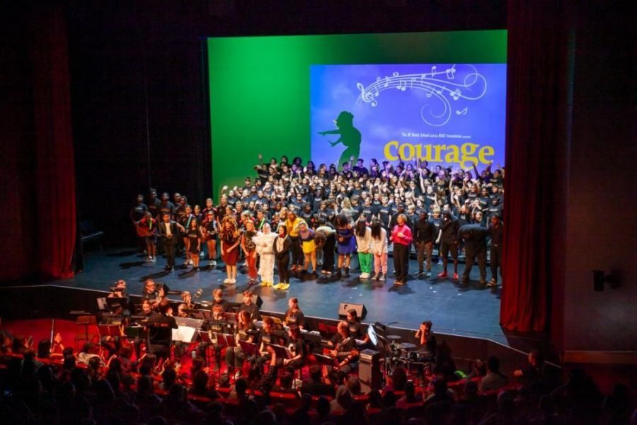 A large group of people are standing on a stage in front of a large screen that says courage.