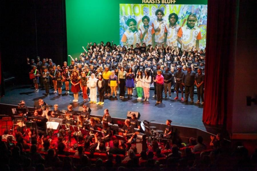 A large group of people are standing on a stage in front of an orchestra.