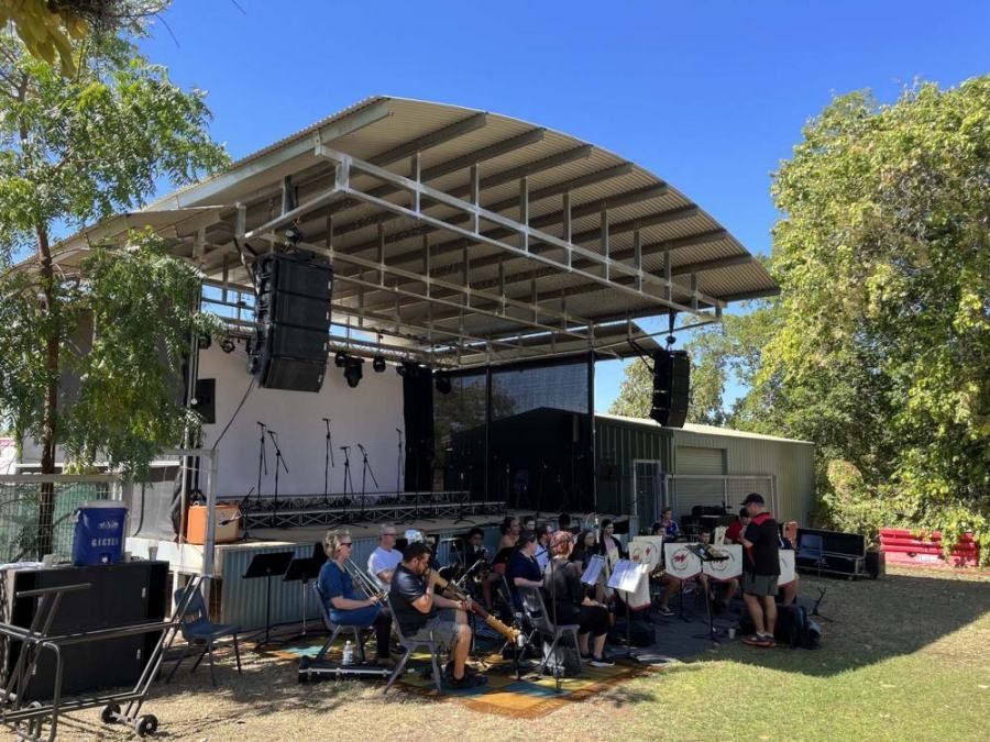 A group of people are sitting in front of a stage in a park.