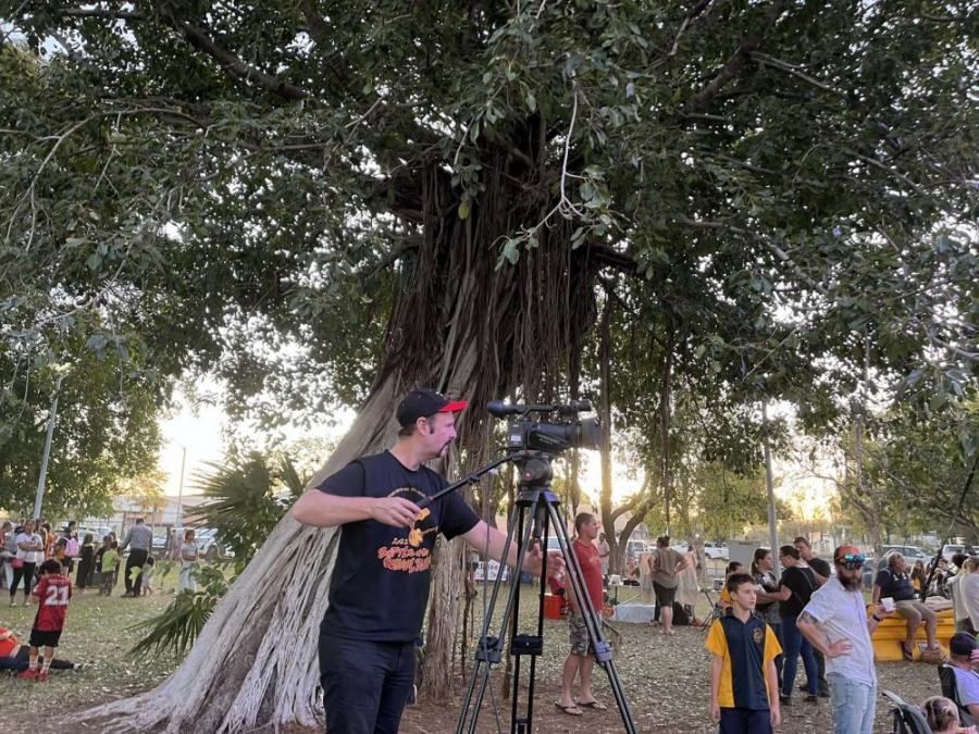 A man is standing in front of a tree with a camera on a tripod.