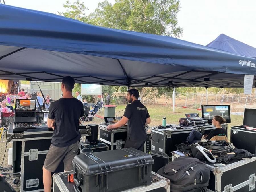 A group of people are standing under a blue tent.