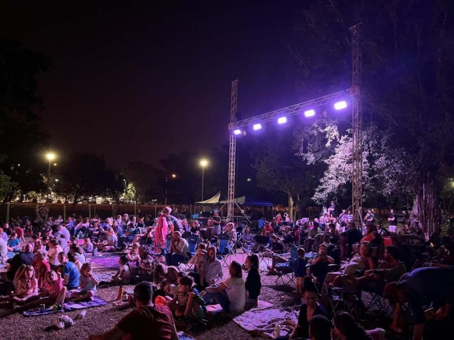 A large group of people are sitting on the ground in front of a stage at night.