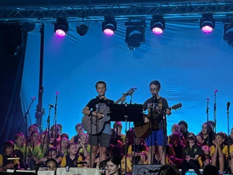 Two boys are playing guitars on a stage in front of a crowd.