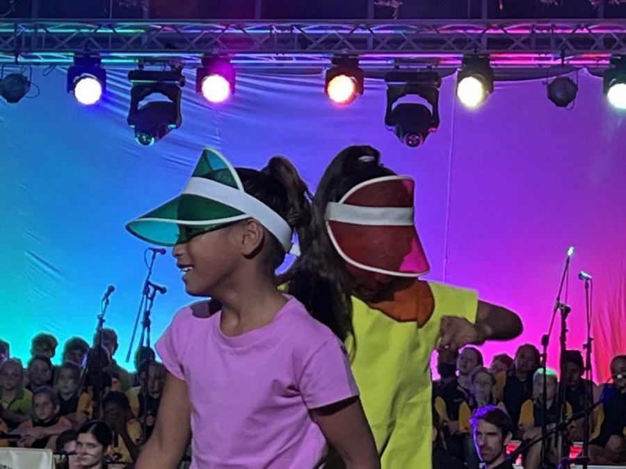 Two girls wearing visors are dancing on a stage in front of a crowd.