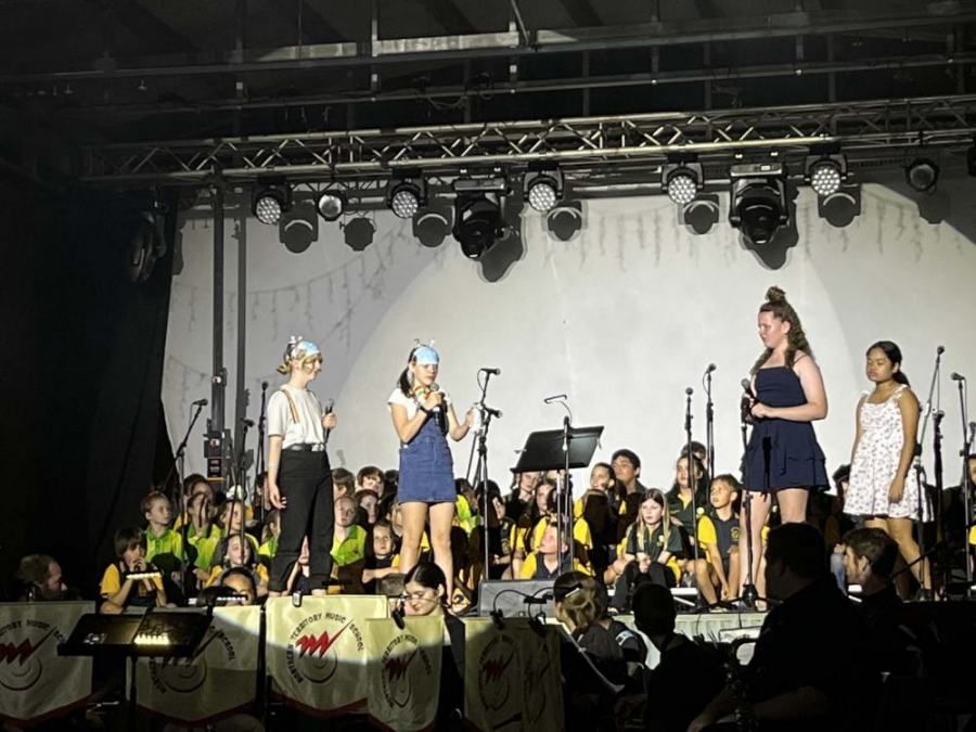 A group of girls are singing on a stage in front of an orchestra.