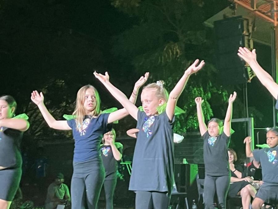 A group of young girls are dancing on a stage with their arms in the air