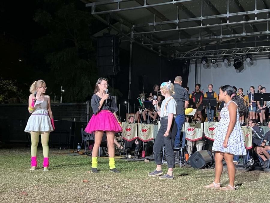A group of women are standing on a stage in front of an orchestra.
