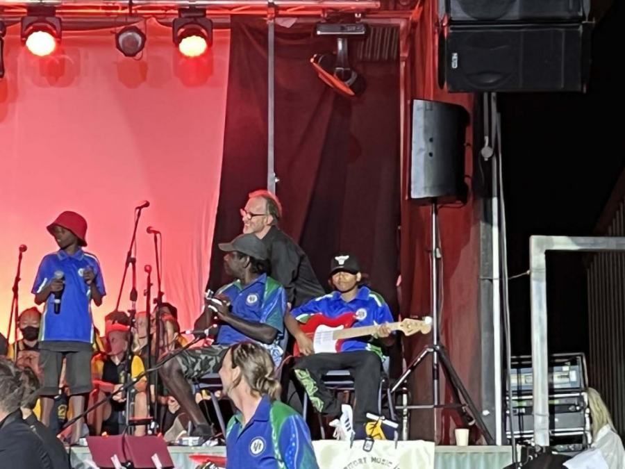 A group of people on a stage with a man playing a guitar with the letter t on it