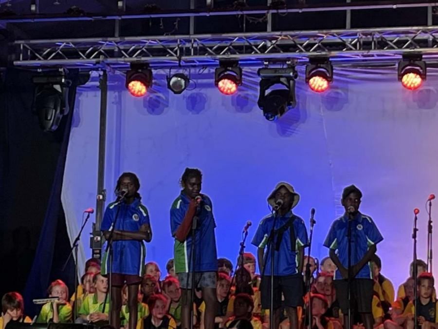 A group of children are singing into microphones on a stage.