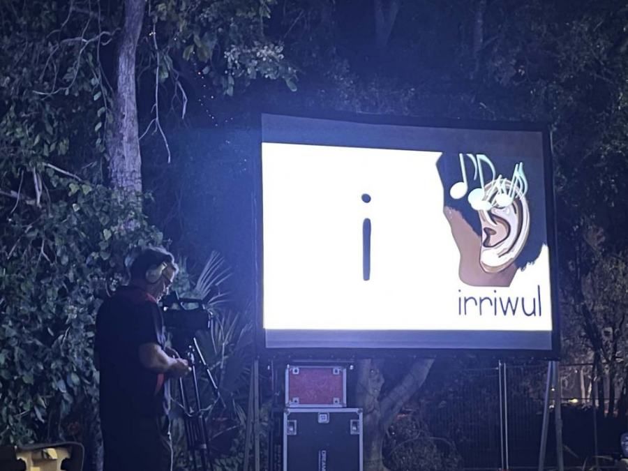 A man stands in front of a large screen that says ' irriwul ' on it