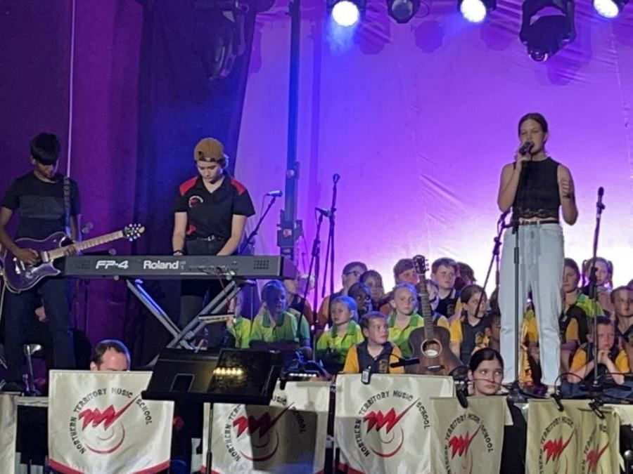 A woman singing into a microphone on a stage in front of a roland keyboard