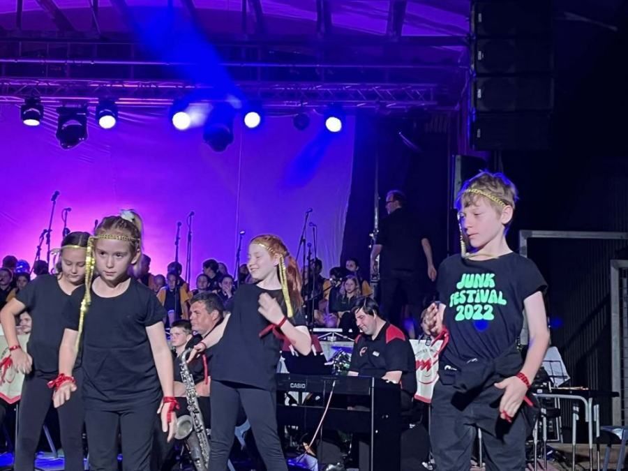 A group of children are dancing on a stage and one of them is wearing a shirt that says june festival 2022