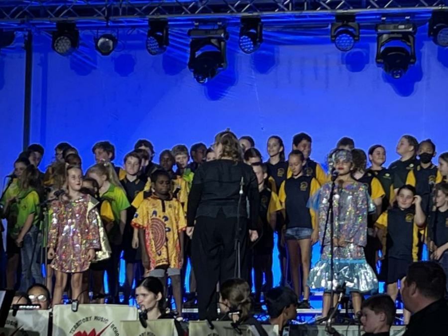 A woman is leading a choir of children on a stage.