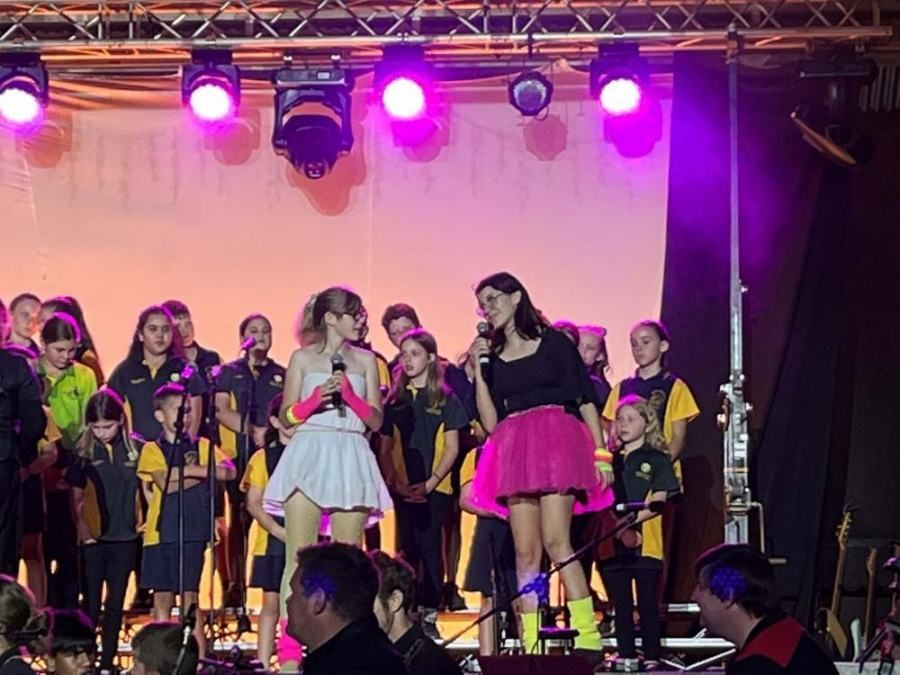 A group of children are singing on a stage with purple lights